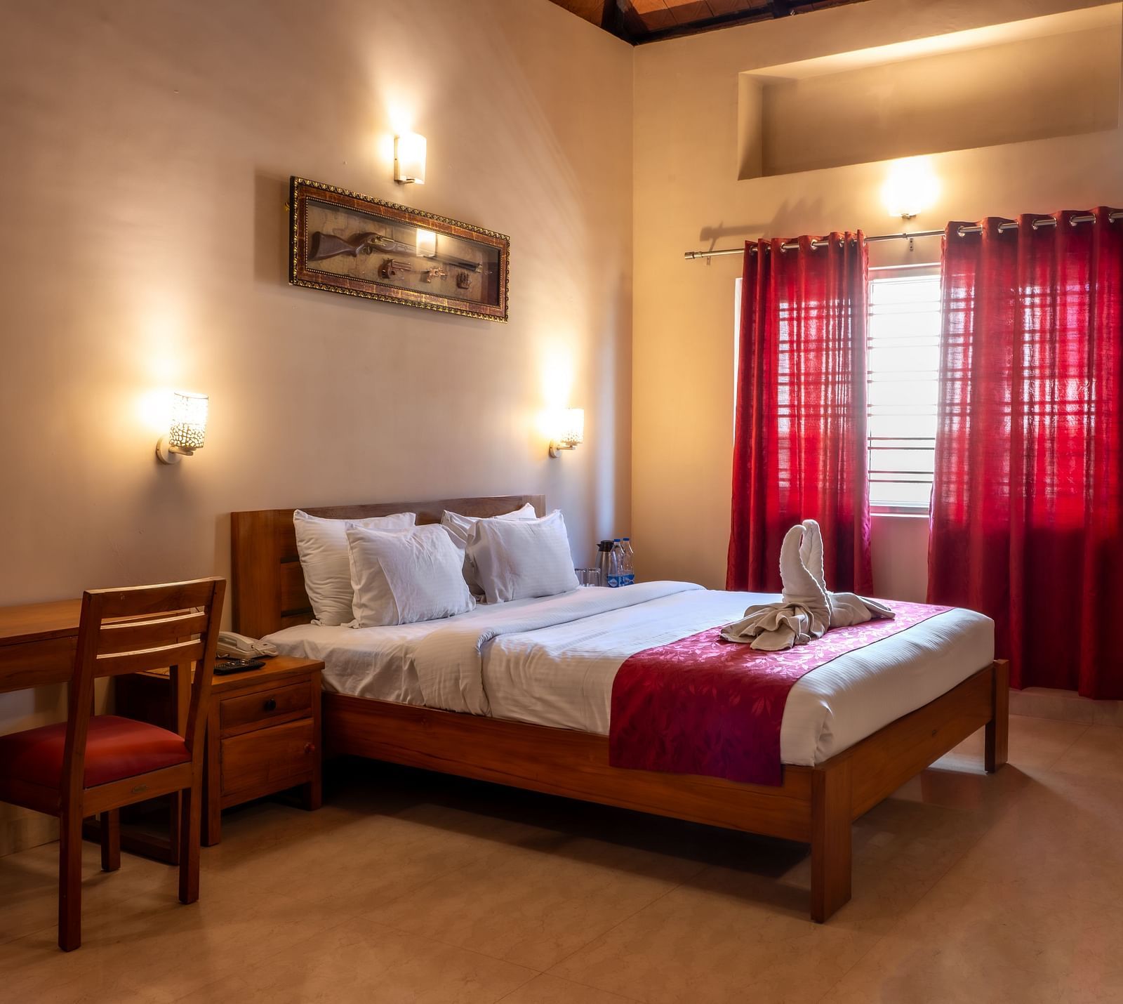 Attic Villa includes a wooden bed with white linens, red curtains, a writing desk, and wall-mounted artwork | Woodstock Resorts, Coorg