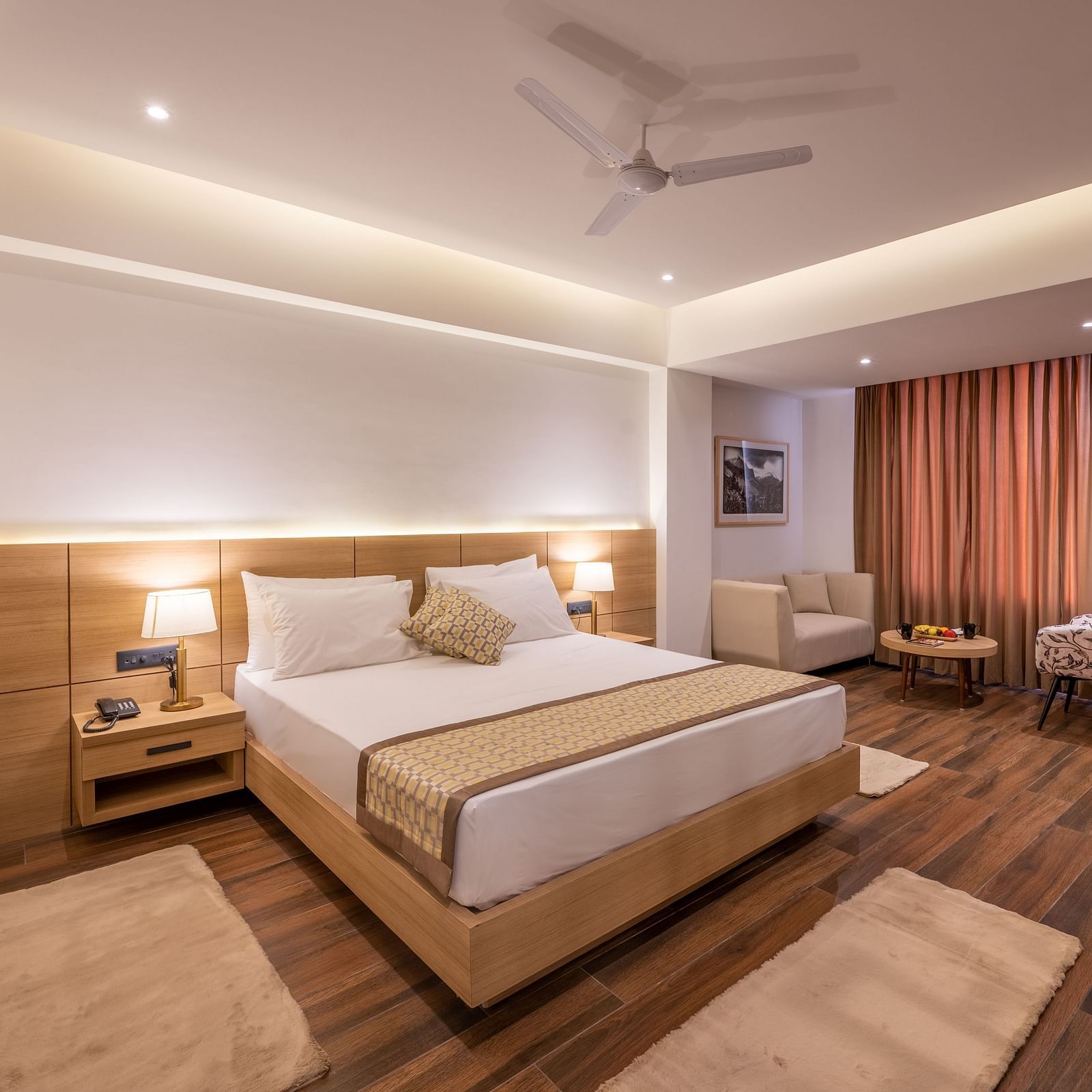 Overview shot of Premium Room at Vishranti Resort, Dehradun featuring a king bed with side tables, a TV, large window and bed lamps. 