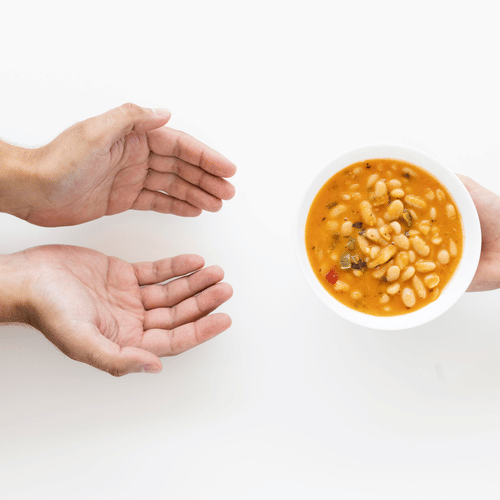 A hand offers a bowl of bean soup to outstretched hands.
