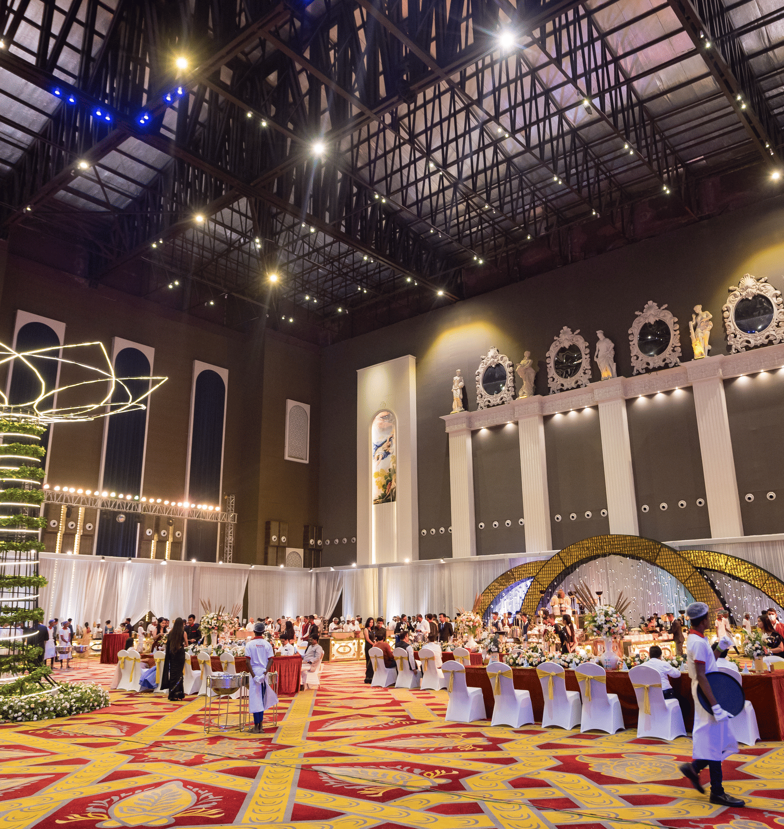 Vast, high-ceilinged convention or banquet hall decorated for an event with a large hanging ornament and a crowd of people at Hotel Hukam's Lalit Mahal.