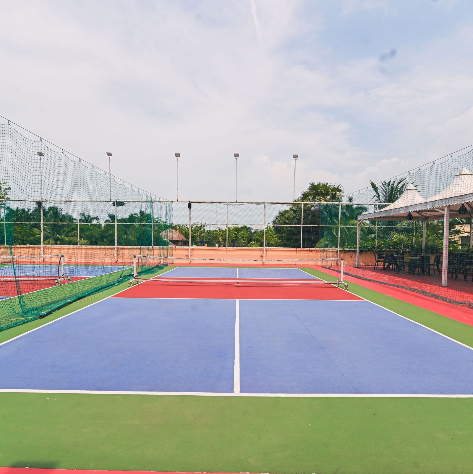 A colourfully painted pickle ball court at Vedic Village Spa Resort under a cloudy sky.