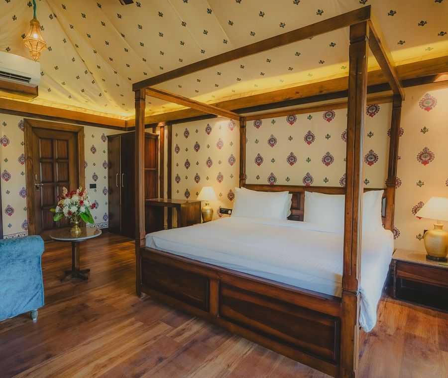 A Premium Duplex Tent bedroom featuring a sofa, a poster bed, bedside table with lamps on either side, cabinet table, a wardrobe, and a centre table with flower vase at The Baagh Ananta Elite, Ranthambore
