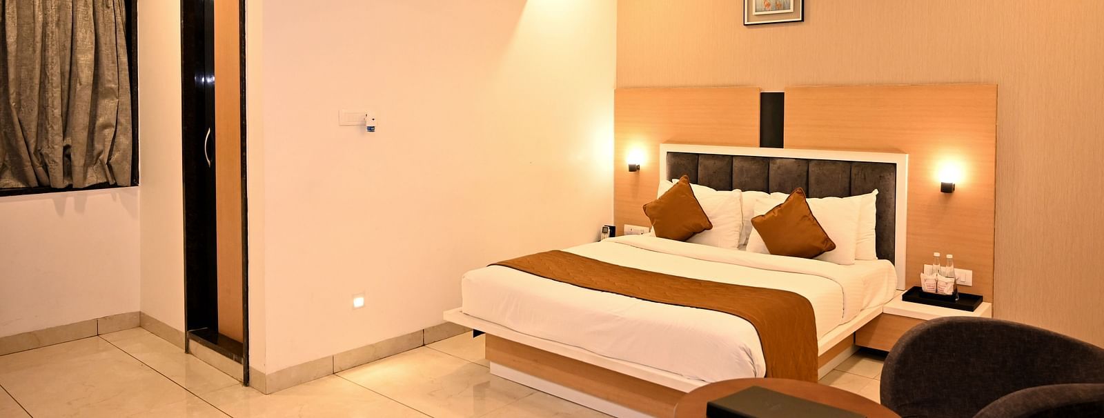 A stylish bedroom featuring a large bed with a green headboard and textured wall art - TGI Insignia, Bhopal
