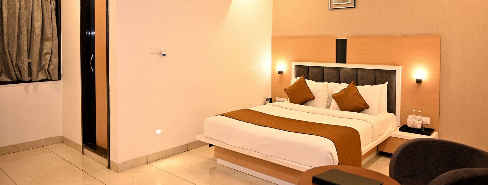 A stylish bedroom featuring a large bed with a green headboard and textured wall art - TGI Insignia, Bhopal