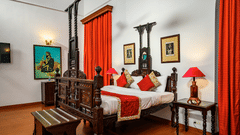 A double bed on a beautifully carved bed from wood, with a lamp on the side inside Maharaja Moninder Singh room - The Baradari Palace