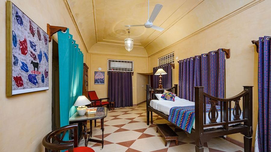 A room with a single bed, a table, seating, and purple curtains dividing the space at Tijara Fort-Palace - 19th Century, Alwar.