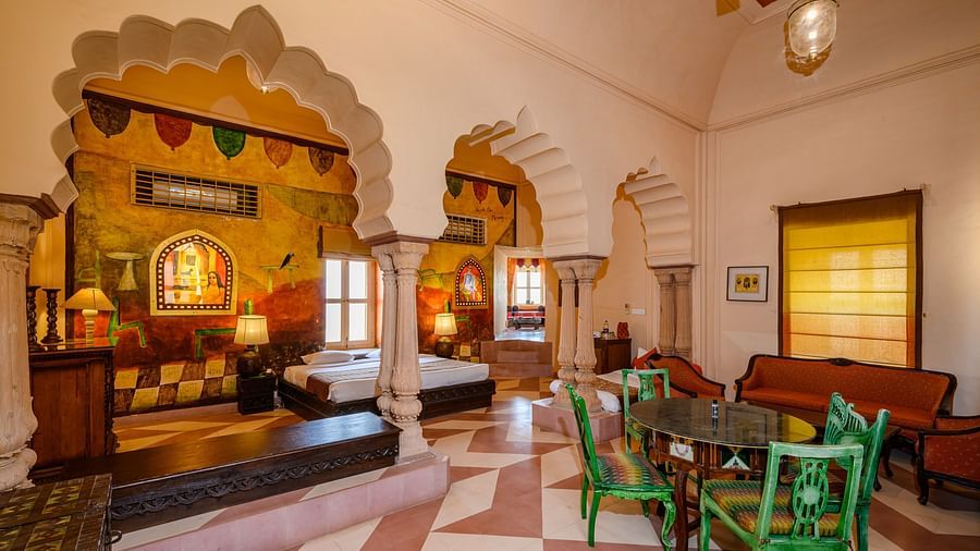 A room with a bed, seating areas, arched architectural details, and a painted mural at Tijara Fort-Palace - 19th Century, Alwar.