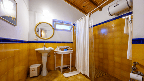 A yellow themed bathroom with wash basin and water heater with separate shower space - Ramgarh Bungalows, Nainital.