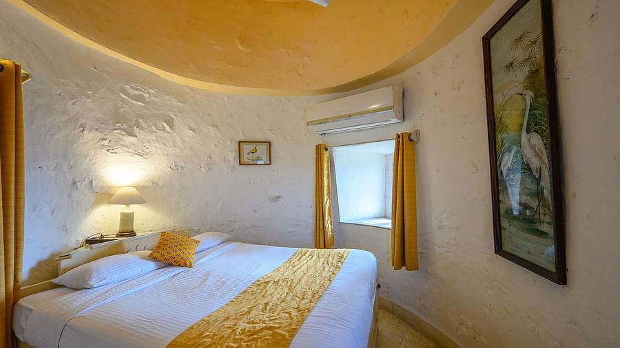 Hill Fort Kesroli 14th Century Alwar - interior view of the Saras Mahal with a king size bed, yellow ceiling and white walls adorned with paintings 