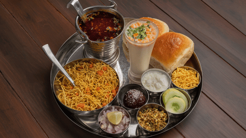 A traditional Indian thali with assorted dishes including rice, dal, vegetables, chutneys, salad, and bread served on a large metal plate.