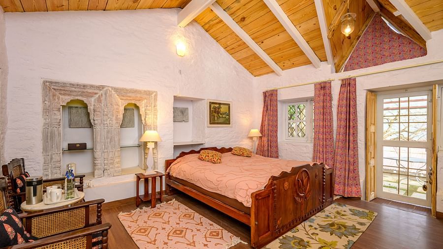 A double bed with chairs on the side inside one of the rooms - Ramgarh Bungalows, Nainital.