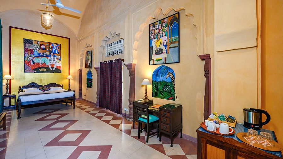A spacious room with a bed, artwork, seating, and a refreshment station at Tijara Fort-Palace - 19th Century, Alwar.