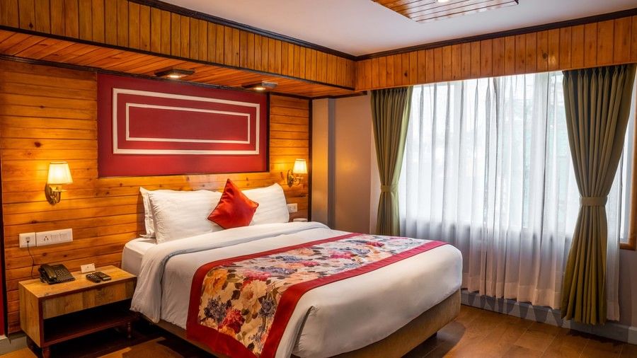 A well-furnished guest room with wooden interiors and a large window with a plushy bed at Mount Conifer Suites & Spa, Darjeeling