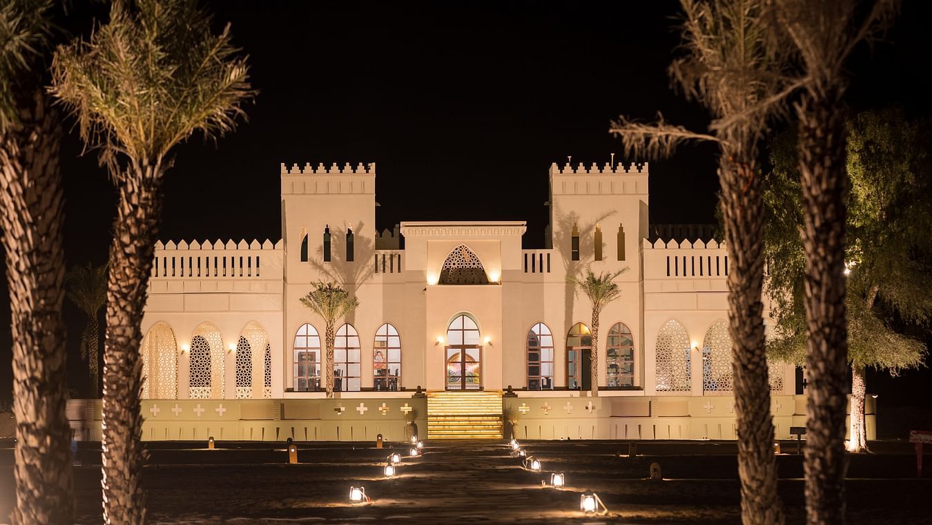 A beautiful view of the hotel facade at night surrounded by palm trees - Karwaan Jaisalmer