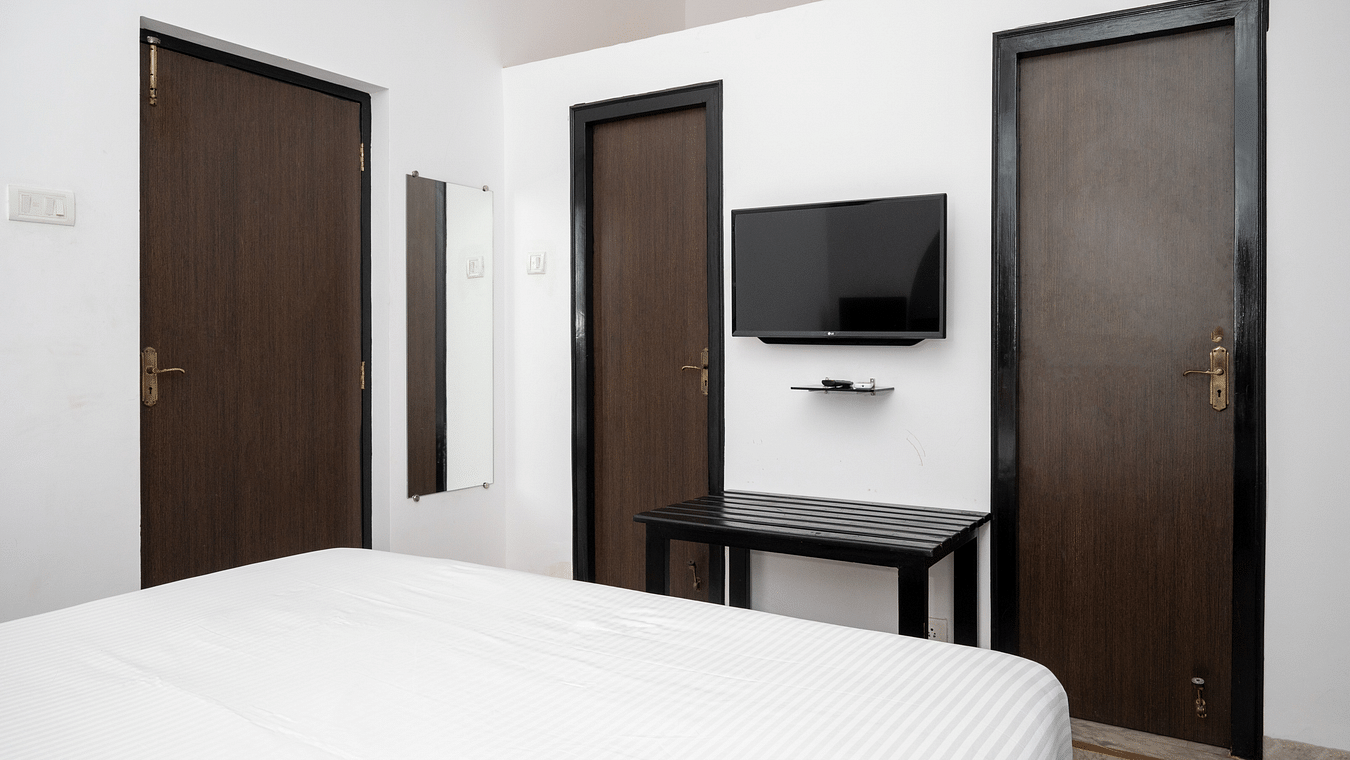 A bed with white linens overlook a wall with a TV and two doors - Richmonde Ananta Elite, Goa