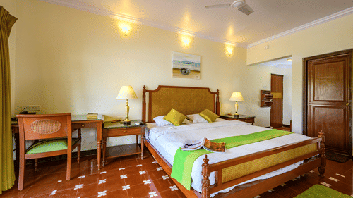 a double bed with a painting above it study table and chair inside Olivia - River View room at neemrana s three waters