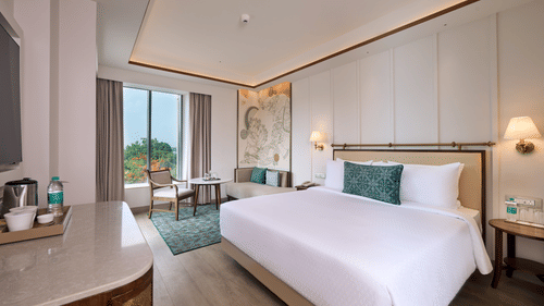 Superior Double Room at Prachi Sarovar Premiere, Bhubaneswar, showing a large bed, a counter space, bedside lamps, a seating area, and a large window.