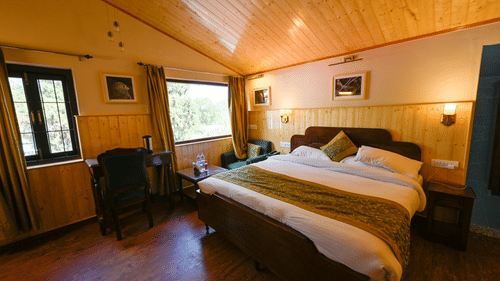 Cosy hotel room with a wooden interior, featuring a king-size bed, large windows, and mountain views.