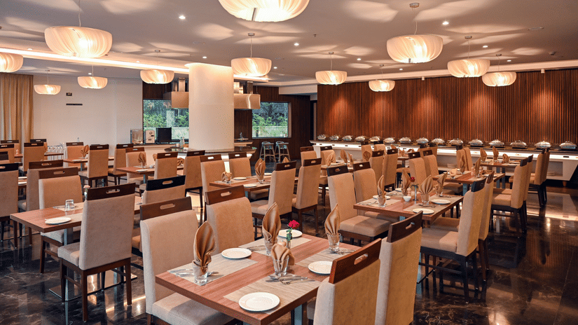 A sitting area at the multi-cuisine restaurant with tables, chairs, and lights at Dimora, Kozhikode.