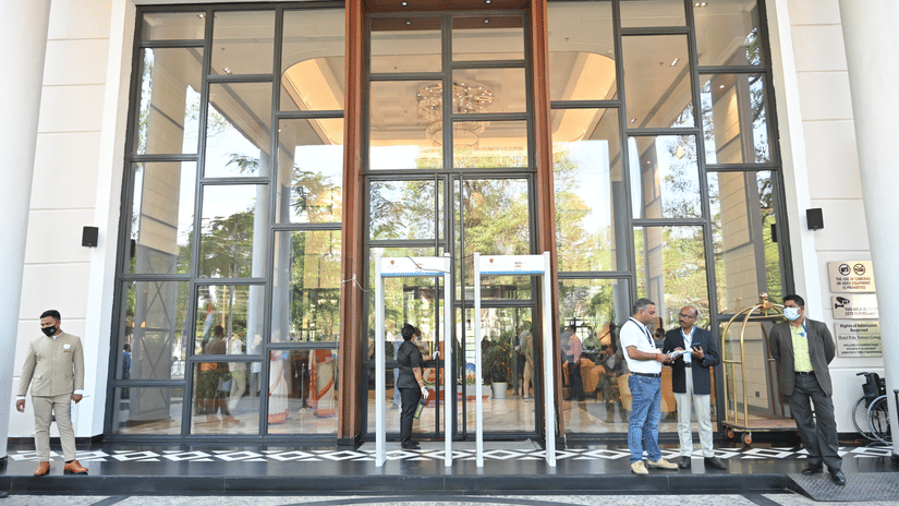 Glass-fronted main entrance of Polo Hotel, Agartala with a bellman, guests entering, a luggage cart, and a checkered marble floor at the porte-cochere.