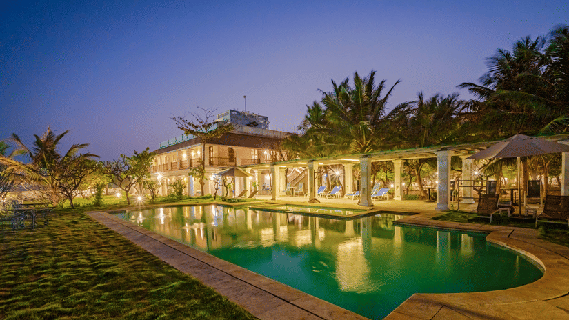 The Bungalow On The Beach in Tranquebar under a vibrant sky near Poompuhar with the pool reflecting the building as the dusk approaches