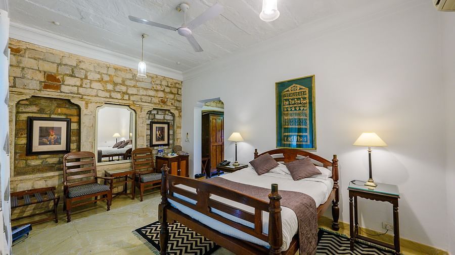  Deo Bagh - 17th Century, Gwalior - the king size bed kept beside the brick wall with wall paintings offered at the Samarjit Vilas - Naubagh / Garden View room in Gwalior