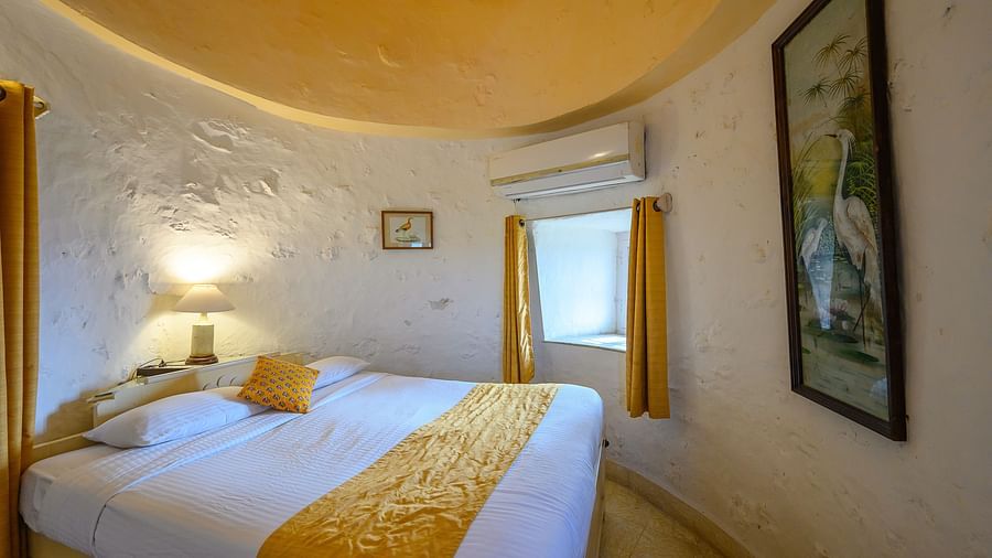 Hill Fort Kesroli 14th Century Alwar - interior view of the Saras Mahal with a king size bed, yellow ceiling and white walls adorned with paintings 