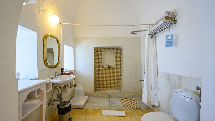 Hill Fort Kesroli 14th Century Alwar - interior view of the Saras Mahal Washroom featuring a commode,  wash basin with a yellow light and a separate shower space 