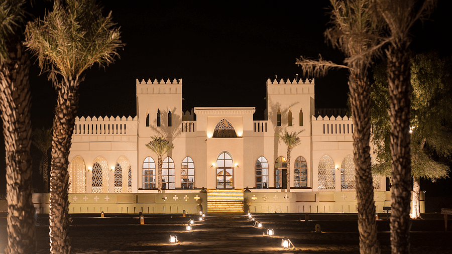 The facade of the hotel surrounded by palm trees at night - Karwaan Jaisalmer