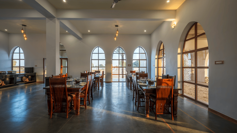 Dining hall at Karwaan resort in Jaisalmer featuring several sets of table and chairs and a buffet section at one corner.