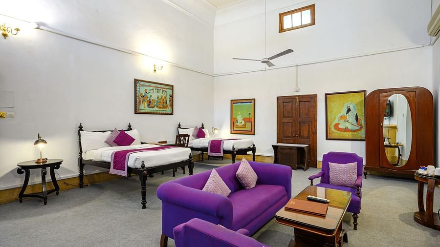 An overview of the Maharaja Karam Singh room with purple sofas, a coffee table and twin double beds- The Baradari Palace