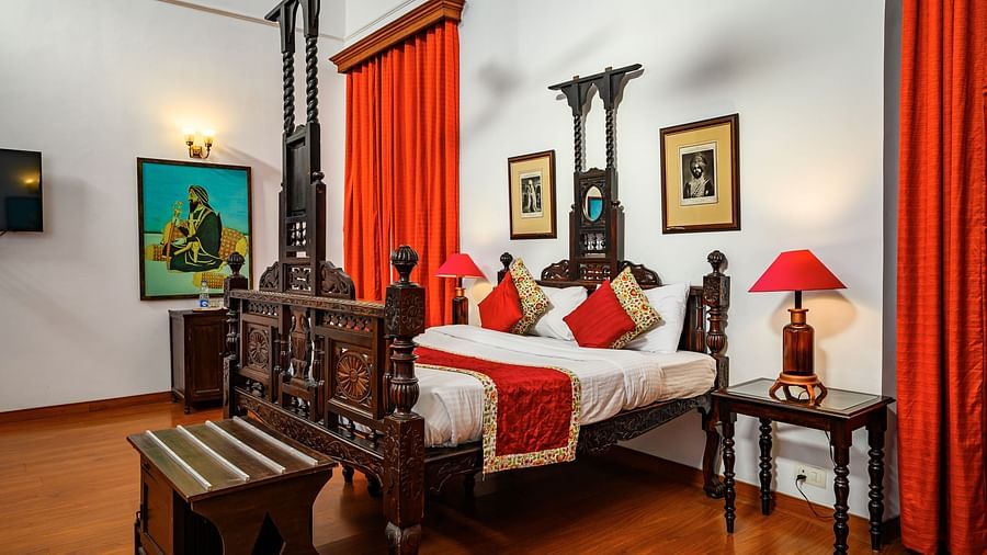A double bed on a beautifully carved bed from wood, with a lamp on the side inside Maharaja Moninder Singh room - The Baradari Palace
