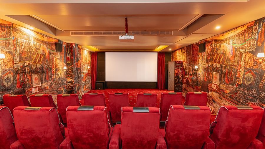 A front angle view of a theatre with a projector hanging from the wall and a large white screen - The Manor Luxury Hotels, Shimla