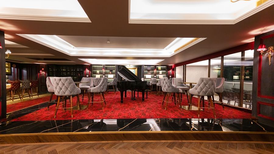 A platform with a tables and chairs placed around a giant piano in Stable restaurant - The Manor Luxury Apartment, Shimla 