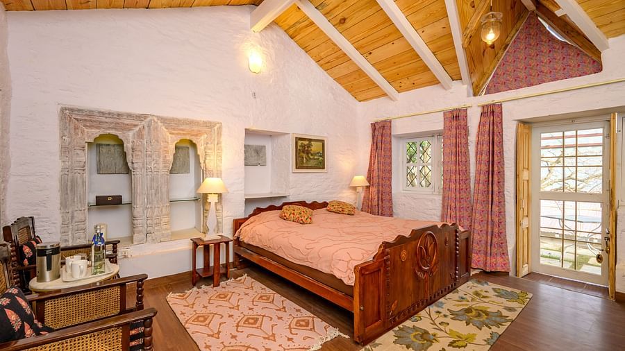 A double bed with chairs on the side inside one of the rooms - Ramgarh Bungalows, Nainital.