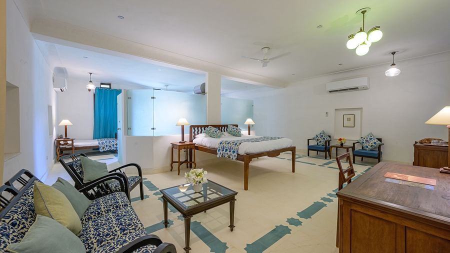 A spacious hotel room with a bed, bedside tables with lamps, multiple seating areas with sofas and chairs around tables, and patterned flooring at Tijara Fort-Palace - 19th Century, Alwar.