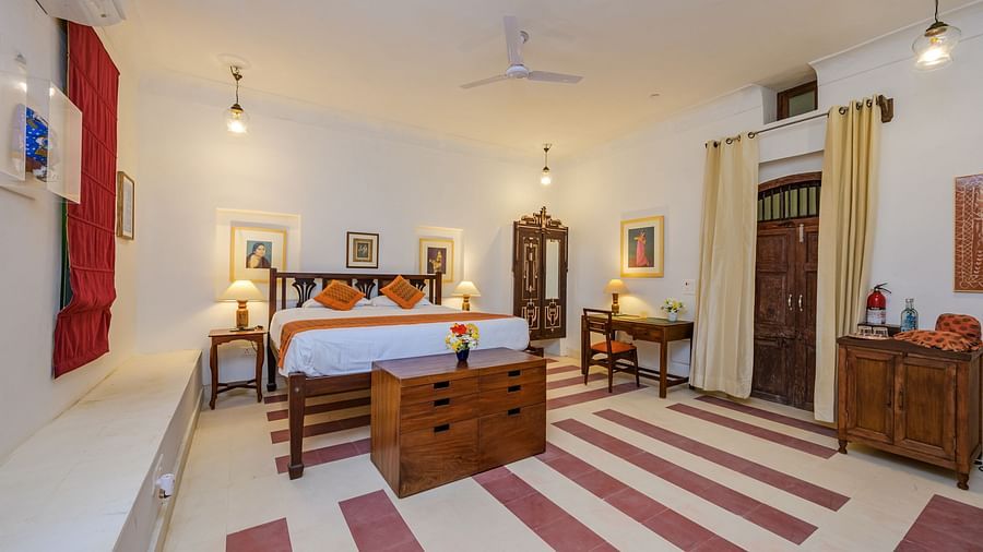 Room with bed, patterned pillows and runner, furniture including desk, chair, dresser, and wardrobe, artwork, decorative ceiling lights, and patterned floor tiles - Tijara Fort-Palace - 19th Century, Alwar.