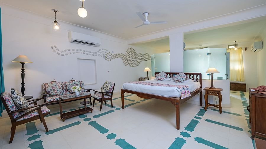 A spacious room with a bed, seating area with a sofa and chairs around a table, patterned floor, and multiple light fixtures at Tijara Fort-Palace - 19th Century, Alwar.
