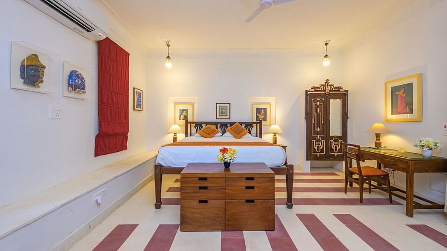 Room with bed, patterned pillows and runner, furniture including desk, chair, dresser, and wardrobe, artwork, decorative ceiling lights, and patterned floor tiles - Tijara Fort-Palace - 19th Century, Alwar.
