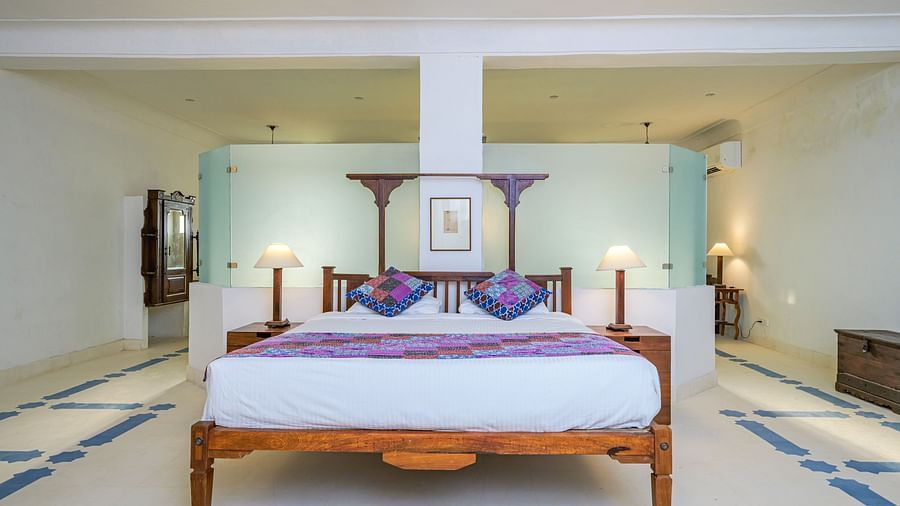 Room with four-poster bed, patterned runner and pillows, furniture including tables, decorative ceiling lights, and patterned floor tiles - Tijara Fort-Palace - 19th Century, Alwar.