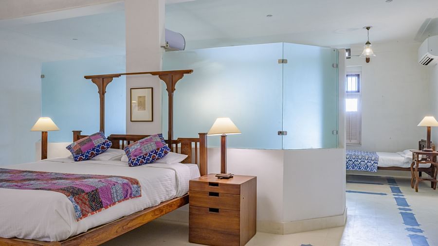 Room with four-poster bed, patterned runner and pillows, furniture including tables, decorative ceiling lights, and view into another room with bed and patterned floor tiles - Tijara Fort-Palace - 19th Century, Alwar.