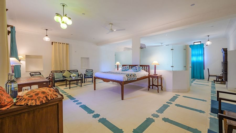 A spacious hotel room with a bed, bedside tables with lamps, a seating area with sofas and chairs around a table, and patterned flooring at Tijara Fort-Palace - 19th Century, Alwar.