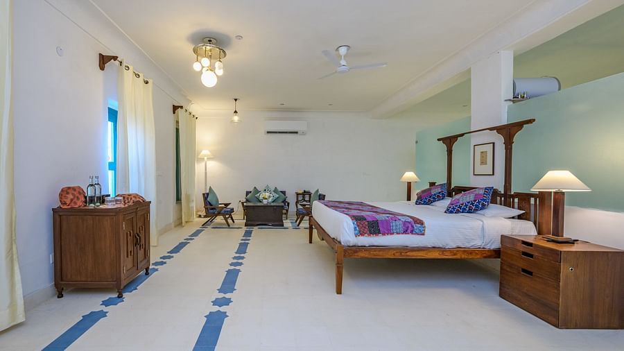 Room with four-poster bed, patterned runner and pillows, furniture including cabinets, tables, and chairs, decorative ceiling lights, and patterned floor tiles - Tijara Fort-Palace - 19th Century, Alwar.