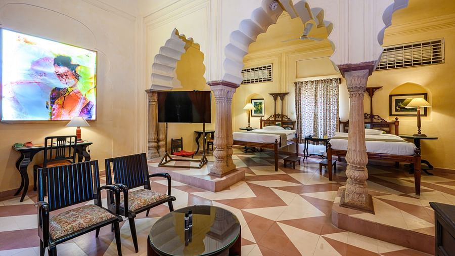A room with two beds, chairs, a table, and a television in Tijara Fort-Palace - 19th Century, Alwar.