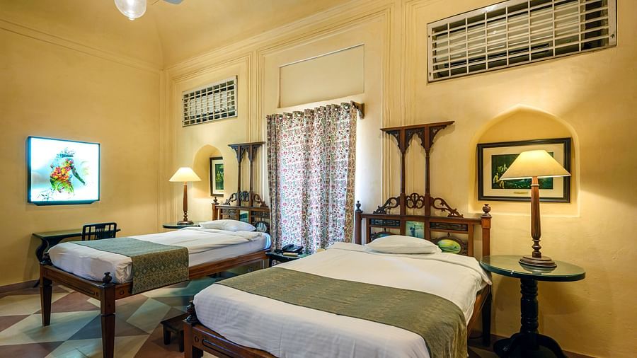 A bedroom with two beds, two side tables with lamps, and a television in Tijara Fort-Palace - 19th Century, Alwar.