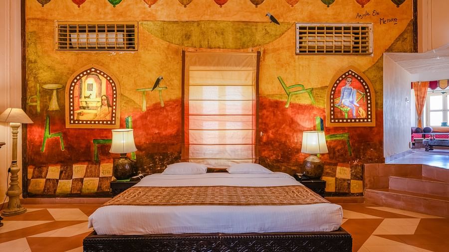A bedroom with a bed, two lamps, and wall art in Tijara Fort-Palace - 19th Century, Alwar.