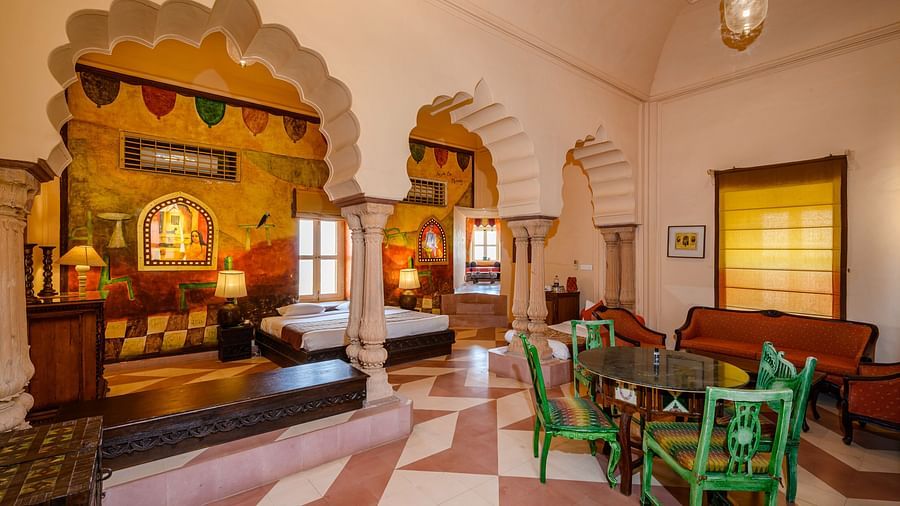 A room with a bed, a table with chairs, and a seating area in Tijara Fort-Palace - 19th Century, Alwar.