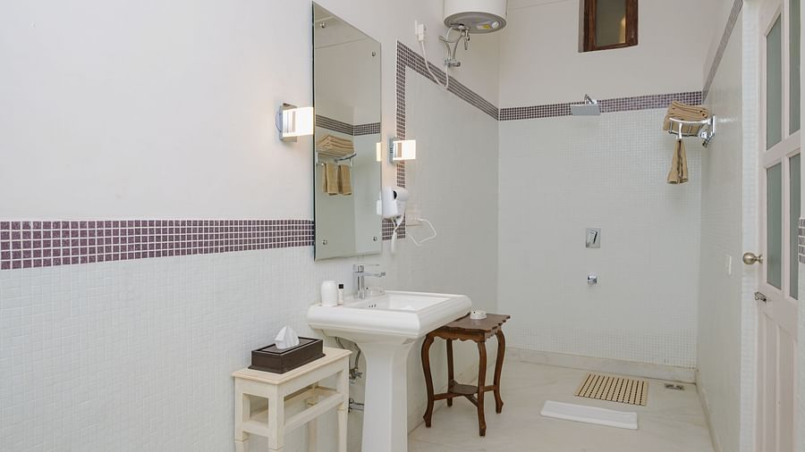 A bathroom with a pedestal sink, a mirror above it, a shower area, and a small stool at Tijara Fort-Palace - 19th Century, Alwar.