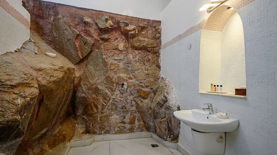 Bathroom with sink, mirror, wall lighting, stone feature wall, and tiled floor - Tijara Fort-Palace - 19th Century, Alwar.