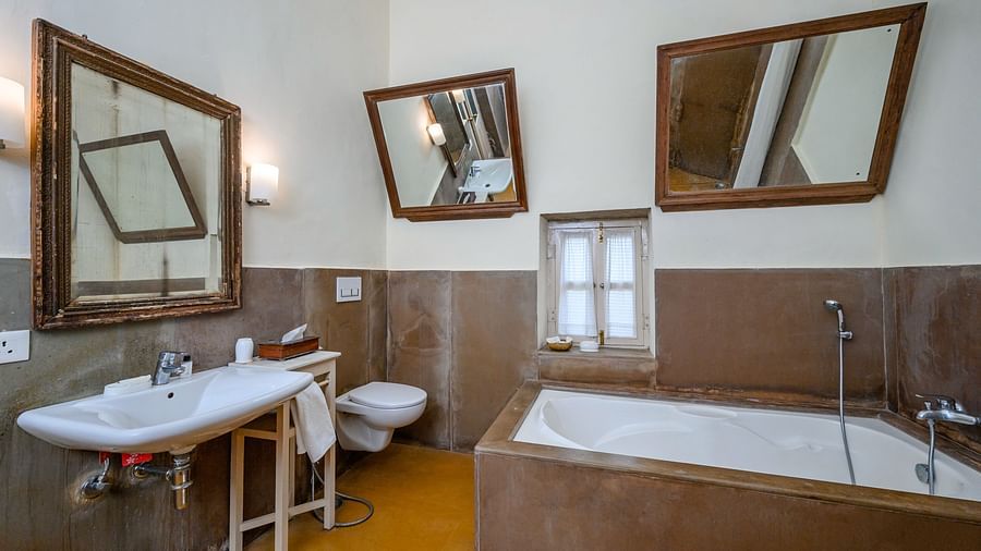 A bathroom with two sinks, three mirrors on the wall, a toilet, and a bathtub at Tijara Fort-Palace - 19th Century, Alwar.